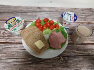 Zdjęcie przedstawia Dietę z ograniczeniem łatwoprzyswajalnych węglowodan&oacute;w: Chleb Graham  Masło extra  Serek wiejski ziarnisty  Kawa zbożowa z mlekiem Jogurt naturalny  Sałata zielona Pomidorki koktajlowe Szynka pieczona na ogniu wieprzowa z dod.wodą, wędzona, pieczona, parzona